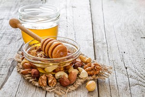 Honey in glass jar and dipper, selection of nuts  on rustic wood background